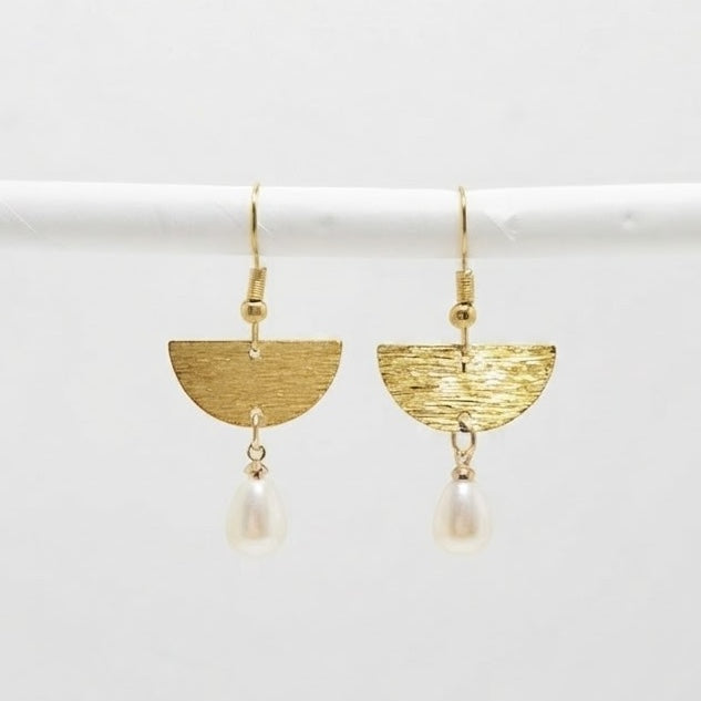 A pair of gold geometric dangle earrings with textured semi-circles and hanging pearl drops, displayed on a white horizontal bar against a light gray background.