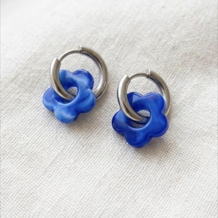 A pair of silver hoop earrings with translucent blue flower charms,.